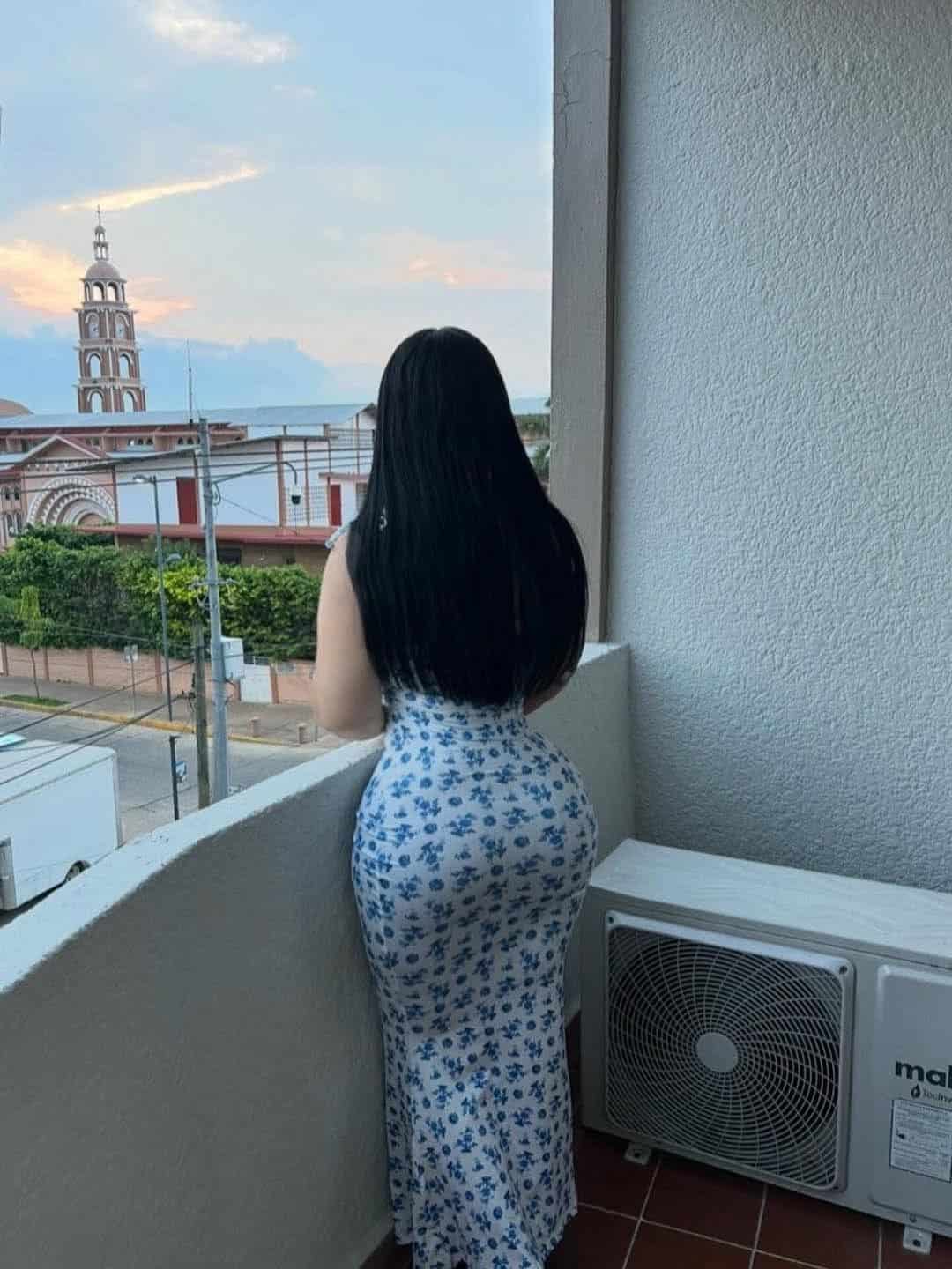 Long-haired beauty call girl sitting by hotel window with night skyline